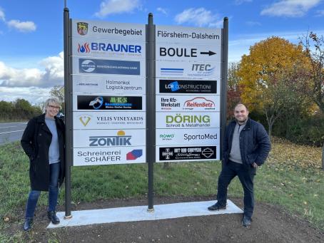VG-Mitarbeiterin Beate Hess und Ortsbürgermeister Tobias Rohrwick an der neuen einheitlichen Hinweisbeschilderung an der Einfahrt des Gewerbegebietes.